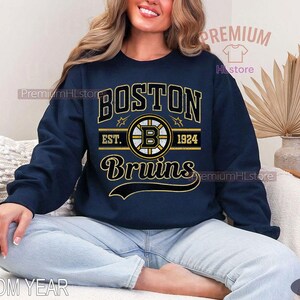 Puede incluir: Sudadera azul marino con el texto "BOSTON Bruins" en letras doradas y blancas. El dise&ntilde;o incluye el logotipo de los Bruins y el a&ntilde;o "1924". Una sudadera cl&aacute;sica de cuello redondo.