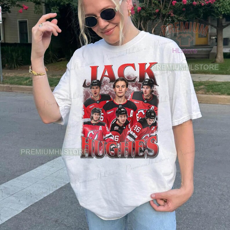 May include: White t-shirt featuring a graphic of hockey players in red and black jerseys. The text "JACK HUGHES" is printed in red above and below the players. The shirt has a vintage, distressed look.