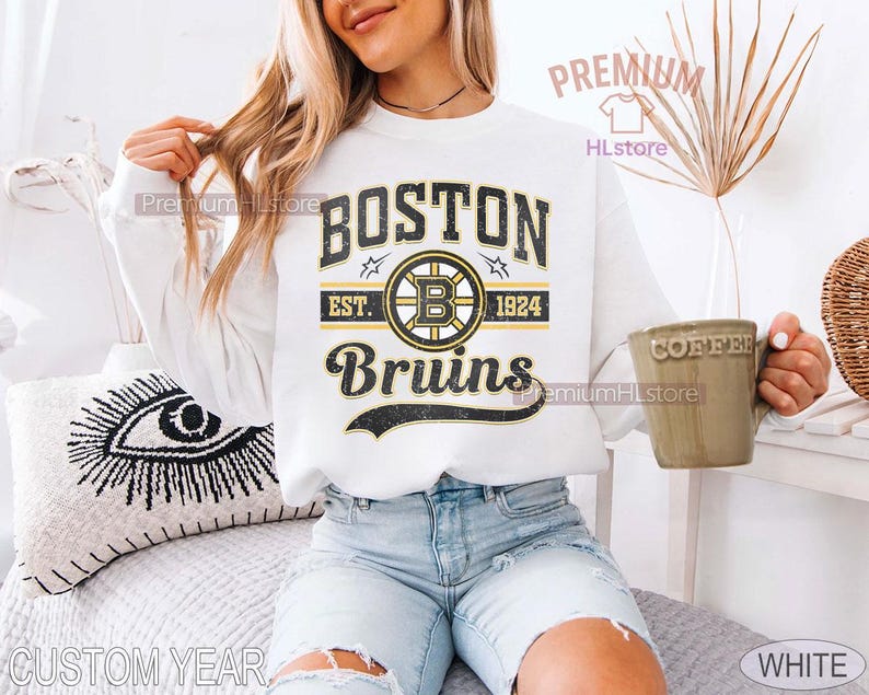 Puede incluir: Sudadera blanca con el texto "BOSTON Bruins EST. 1924" en negro y dorado. El dise&ntilde;o incluye un logotipo de los Bruins. La sudadera es de estilo casual, adecuada para los fan&aacute;ticos del deporte.