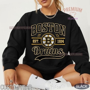 Puede incluir: Sudadera negra con el texto "BOSTON Bruins" en dorado y blanco, con el logotipo del equipo y "EST. 1924". La sudadera tiene cuello redondo y mangas largas. Tambi&eacute;n se ven las palabras "CUSTOM YEAR" y "BLACK".