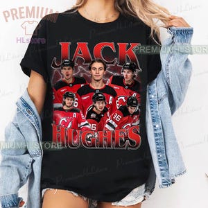 May include: Black t-shirt featuring a graphic of hockey players in red and black jerseys. The text "JACK HUGHES" is printed in red and white. The shirt has a vintage, distressed look.