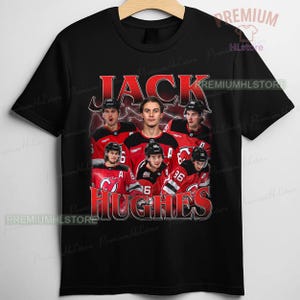 May include: Black t-shirt featuring a graphic of a hockey player and the name "JACK HUGHES" in red. The design includes a group of hockey players in their team uniforms. The shirt has a crew neck and short sleeves.