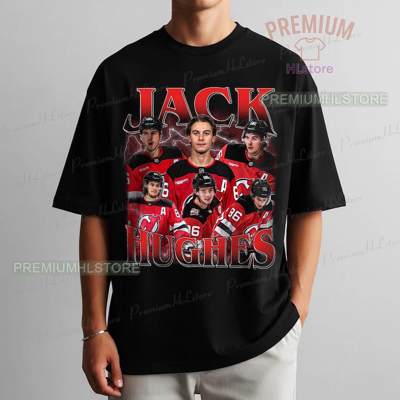 May include: Black t-shirt featuring a graphic of Jack Hughes and other hockey players in red and black jerseys. The name "JACK HUGHES" is printed in red, stylized text above the players. The shirt has a crew neck and short sleeves.