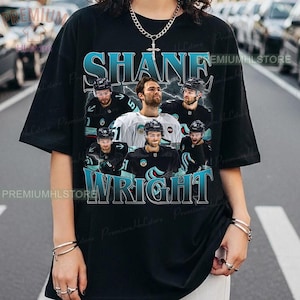 May include: Black t-shirt featuring a graphic of Shane Wright, a hockey player, with the text "SHANE WRIGHT" in teal and white. The design includes multiple images of the player in his hockey uniform.