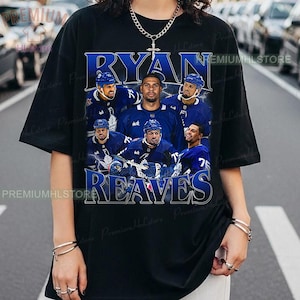 May include: Black t-shirt with a blue graphic of a hockey player and the text "RYAN REAVES". The design includes multiple images of the player in his hockey uniform. The shirt has a crew neck and short sleeves.