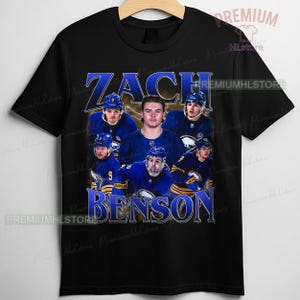 May include: Black t-shirt featuring a graphic of Zach Benson, a hockey player, with his name in blue and white text. The design includes images of the player and other team members in blue and white uniforms. The shirt has a crew neck.