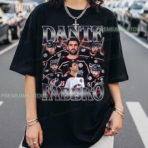 May include: Black t-shirt featuring a graphic of a hockey team with the text "DANTE FABBRO" in a vintage style. The design includes images of players in their jerseys, with a lightning bolt effect.