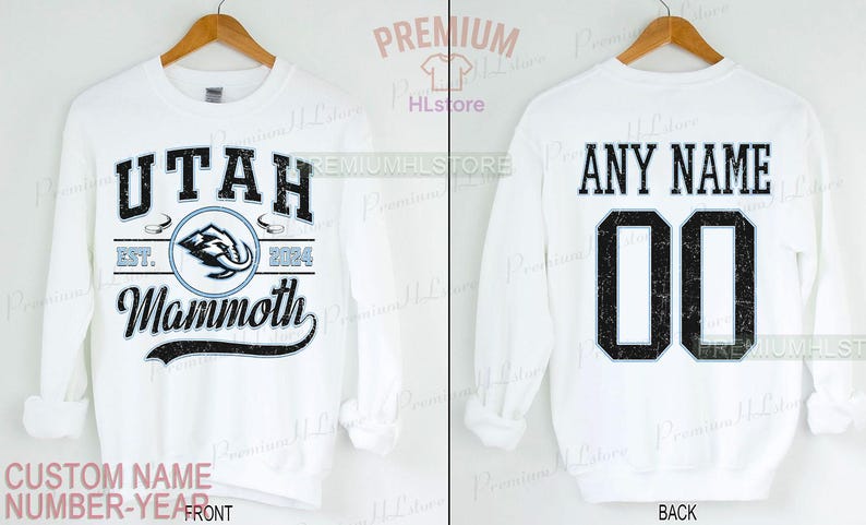K&ouml;nnte beinhalten: Wei&szlig;es Sweatshirt mit "UTAH Mammoth" Text und Logo auf der Vorderseite, mit "EST. 2004" und einer Mammut-Grafik. Auf der R&uuml;ckseite steht "ANY NAME" &uuml;ber der Nummer "00". Das Sweatshirt wird auf einem Holzb&uuml;gel pr&auml;sentiert.