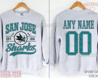 May include: Sport grey sweatshirt with the San Jose Sharks logo and text. The front says "SAN JOSE Sharks" with "EST. 1991". The back has space for a custom name and number. The colour is sport grey.