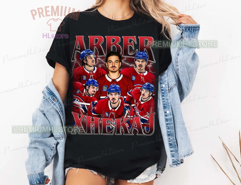 May include: Black t-shirt featuring a vintage-style graphic of a hockey team. The design includes the names "ARBER" and "XHEKAJ" in red and white lettering, along with images of the players in their red and blue uniforms.