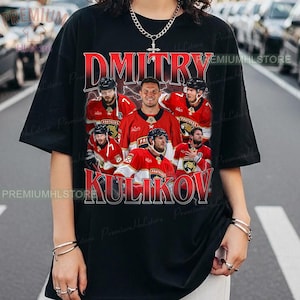 May include: Black t-shirt featuring a graphic of hockey players in red jerseys. The text "Dmitry Kulikov" is displayed in red and white. The shirt has a vintage design and the words "Premium H L Store" are printed on the side.