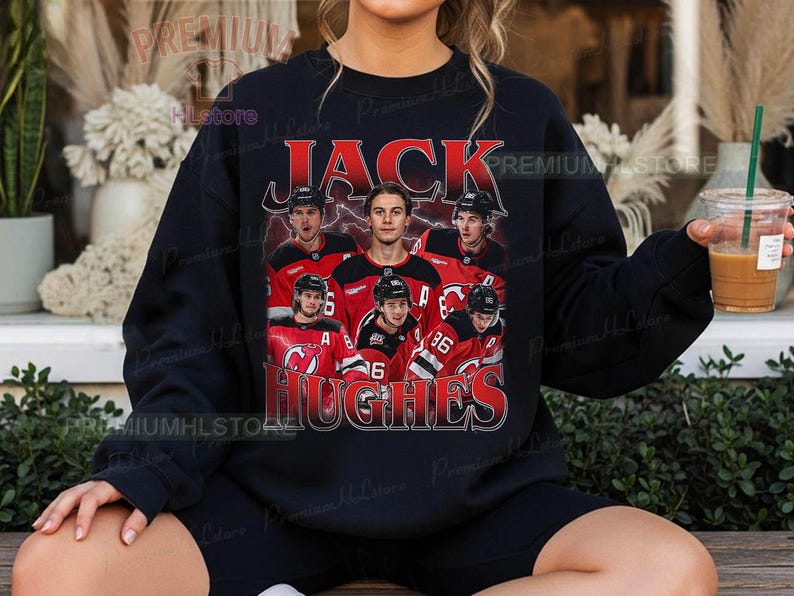 May include: Black sweatshirt featuring a graphic of a hockey player and the text "JACK HUGHES" in red. The design includes images of the player in a red and black jersey. The sweatshirt is a casual style.