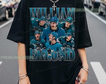 May include: Black t-shirt featuring a graphic of hockey players in teal and blue uniforms. The shirt displays the name "WILLIAM EKLUND" in a stylized font. The image includes the logo of the San Jose Sharks.