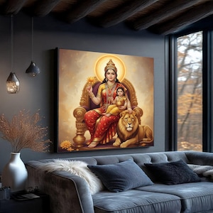 Puede incluir: Una obra de arte enmarcada que representa a una mujer y un niño sentados en un trono con un león. La mujer lleva un sari rojo y dorado, sosteniendo una flor de loto. La obra de arte se exhibe sobre un sofá gris en una sala de estar.