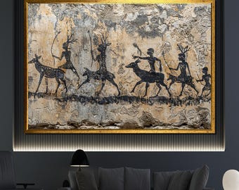 May include: A framed artwork depicting a prehistoric hunting scene. The image features black silhouettes of figures with bows and arrows, chasing deer across a textured, beige and gray background. The artwork is encased in a gold frame.
