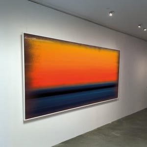 Puede incluir: Gran pintura abstracta enmarcada. La obra presenta un degradado de colores, con naranja en la parte superior, rojo en el medio y una banda azul oscuro en la parte inferior. La obra se exhibe en una pared blanca.