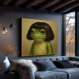 May include: A framed artwork featuring a green frog with large eyes and a dark brown bob haircut. The frog is depicted in a portrait style, set against a neutral background. The artwork is displayed in a living room setting.