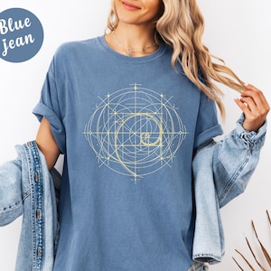 以下が含まれることがあります： 黄金のスパイラルデザインのブルージーンズカラーのTシャツ。デザインは、中央にスパイラルがある幾何学模様です。シャツは半袖でリラックスしたフィット感です。