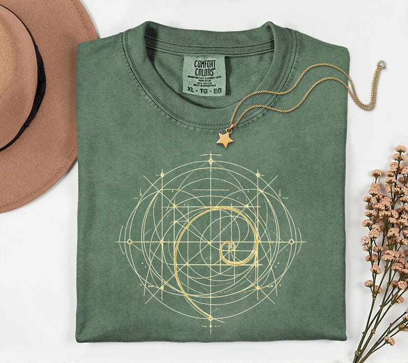 以下が含まれることがあります： セージグリーンのComfort Colors Tシャツ、ゴールドの幾何学模様。ゴールドの星型ペンダントネックレスがシャツの上にあります。シャツには「Comfort Colors」とサイズ「XL」と書かれたタグが付いています。