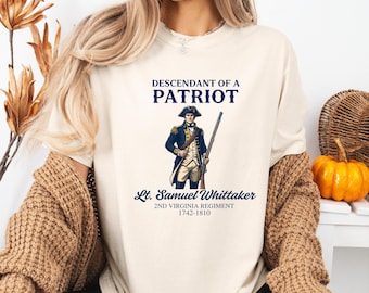 May include: Cream-colored t-shirt featuring the text "DESCENDANT OF A PATRIOT" above an illustration of a soldier in a blue coat and tricorn hat, holding a rifle. Below the illustration is "Lt. Samuel Whittaker 2ND VIRGINIA REGIMENT 1742-1810".