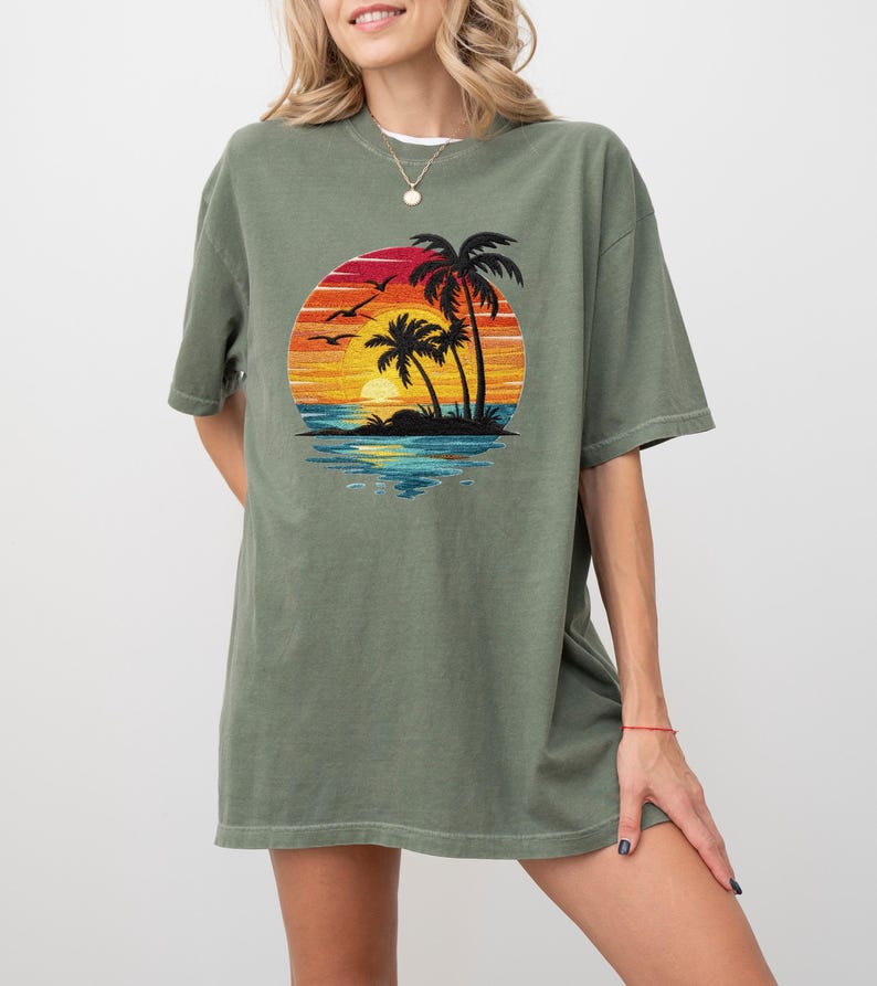 May include: Olive green t-shirt featuring a circular graphic of a sunset over the ocean with palm trees and birds. The graphic has vibrant colors of red, orange, yellow, and blue. The shirt has short sleeves and a relaxed fit.
