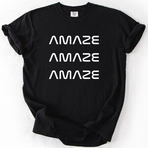 Pu&ograve; includere: T-shirt nero con la parola "AMAZE" stampata tre volte in bianco, impilata verticalmente. La maglietta ha un girocollo e maniche corte. Il tessuto sembra morbido e confortevole.