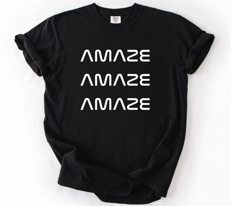 Pu&ograve; includere: T-shirt nero con la parola "AMAZE" stampata tre volte in bianco, impilata verticalmente. La maglietta ha un girocollo e maniche corte. Il tessuto sembra morbido e confortevole.
