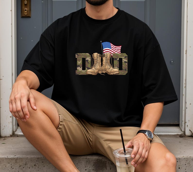 May include: Black t-shirt with the word "DAD" in a camouflage pattern, featuring combat boots and an American flag. The shirt is a relaxed fit, suitable for casual wear. The design is patriotic and celebrates fathers.