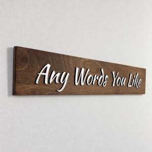 May include: A rectangular wooden sign with a dark brown stained finish featuring the white three-dimensional text Any Words You Like attached to the front surface. The sign is oriented horizontally and displays a smooth wood grain texture.