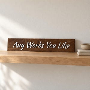 May include: A rectangular dark brown wooden sign featuring the white text Any Words You Like in a cursive font. The sign is positioned horizontally on a light-colored wooden surface, showcasing a smooth finish and clear, legible lettering.