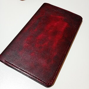 May include: A burgundy leather wallet with a textured surface. The wallet is rectangular and appears to be closed. A leather crafting tool with a wooden handle and a metal blade is in the background.