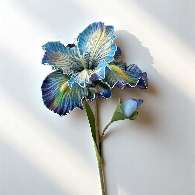 May include: A single artificial blue and green iris flower with a bud. The flower has a ruffled texture and is on a green stem.
