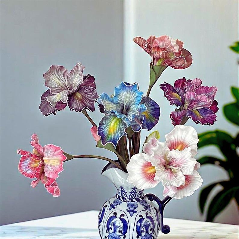 May include: A bouquet of six artificial iris flowers in a blue and white ceramic vase. The flowers are in shades of pink, purple, blue, and white.
