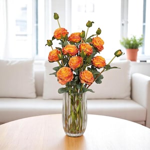 May include: A bouquet of orange and yellow artificial roses in a clear glass vase with vertical lines. The vase is sitting on a wooden table.