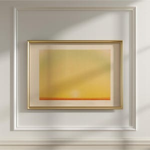 Pode incluir: Uma impressão de arte abstrata emoldurada com uma moldura dourada. A obra apresenta um gradiente de tons amarelos e laranja, com uma linha horizontal laranja na parte inferior. A impressão é montada em um passe-partout creme e em uma parede branca.