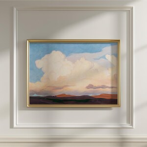 May include: A framed landscape painting featuring a dramatic sky with large, fluffy clouds in shades of white, peach, and pink against a blue backdrop. The foreground depicts a dark, rolling terrain. The gold frame adds a touch of elegance.
