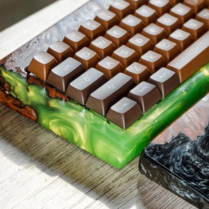 May include: Close-up of a custom mechanical keyboard with brown keycaps and a wooden frame. The frame is accented with green and brown resin. A second keyboard base with a black and brown resin design is also visible.