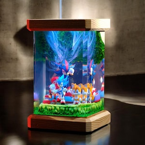 May include: A decorative display featuring Sonic the Hedgehog and friends. The figures are set inside a clear, rectangular case with a wooden base and top. The scene includes a green base, blue sky, and various characters.
