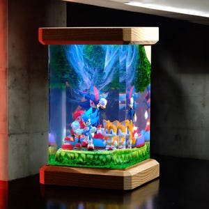 May include: A decorative display featuring Sonic the Hedgehog and friends. The figures are set within a clear, rectangular case with a wooden base and top. The scene includes Sonic, Tails, and Shadow, set against a backdrop of a forest and blue swirls.