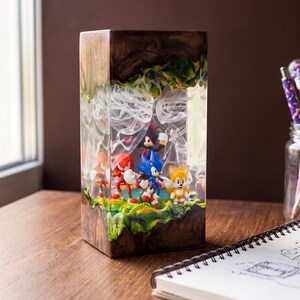 May include: A rectangular resin art piece featuring Sonic the Hedgehog characters. The artwork has a wooden base and a clear resin top with a smoky effect. The characters are set on a green and yellow landscape.