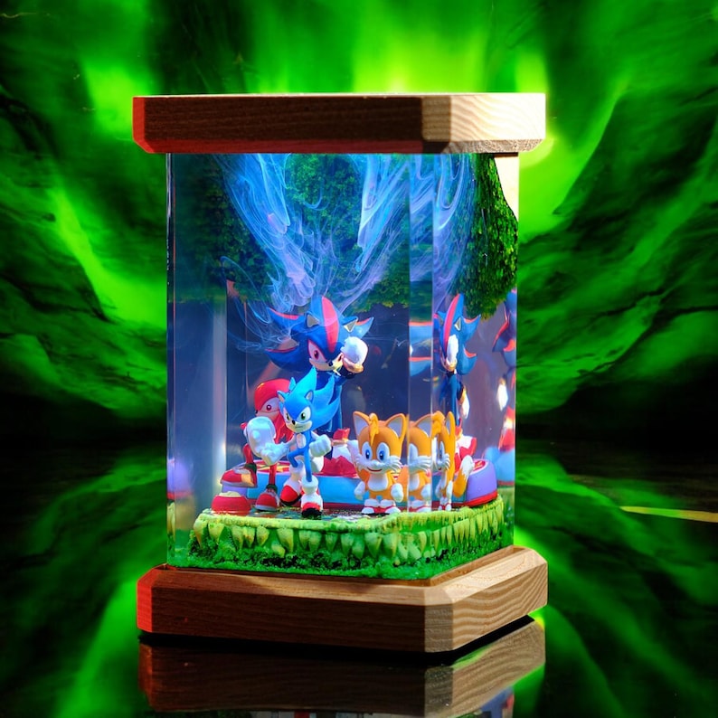 May include: A rectangular display case with a wooden base and top, showcasing Sonic the Hedgehog characters. The case features a green grassy base with figurines of Sonic, Tails, and Shadow. The background has a blue and white swirling design.