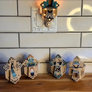 May include: Four cross-shaped ceramic night lights with beige bases and hand-painted designs in blue, black, and brown. One night light is plugged into a wall outlet, while three others are arranged in a row, each featuring unique patterns.