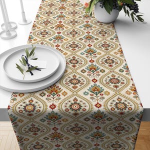 Puede incluir: Un camino de mesa blanco con un patrón repetido de diseños florales coloridos. El patrón presenta una mezcla de colores rojo, amarillo, verde, azul y marrón.