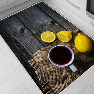 May include: A rectangular kitchen rug featuring a rustic design. The rug displays a dark wood-grain pattern with a cup of dark liquid, lemons, and a burlap texture. The lemons are yellow, and the cup has a light blue handle.