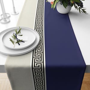 May include: A white and navy blue table runner with a black and white geometric pattern. The runner is made of a linen fabric and has a fringe edge.