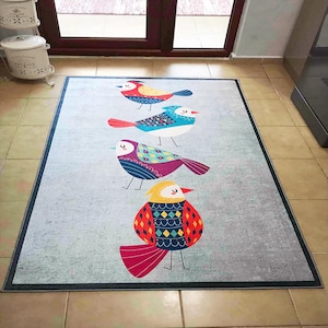 May include: A gray rug with a colorful design of four birds. The birds are all different colors and have different patterns on their bodies. The rug has a light gray background with a subtle texture.