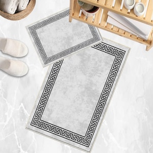Puede incluir: Juego de dos alfombras de baño. Las alfombras son de color gris claro con un borde negro de greca. La alfombra más grande es rectangular, y la más pequeña también. Las alfombras están sobre una superficie similar al mármol.