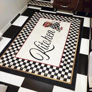 May include: A white kitchen rug with a black and white chequered border. The rug has a red and gold border and the word "Kitchen" written in black cursive. There is a floral design in the centre of the rug.