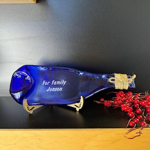 May include: A blue glass bottle, repurposed as a serving dish, with a wooden stand. The bottle is engraved with the text "For family Jonson".