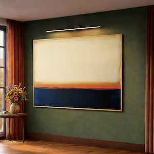 May include: An abstract painting with a gold frame hangs on a dark green wall. The artwork features a cream-colored upper section, a band of orange and red, and a deep blue lower section. A black light fixture is mounted above the painting.